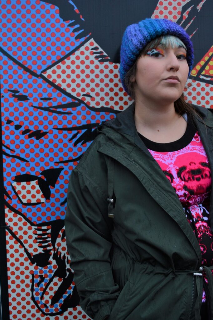 A teen girl with attitude leaning against a wall painted with a cartoon mural